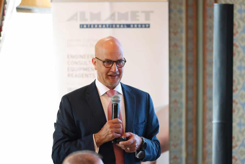 Speaker addressing the participants in front of the ALMAMET International Group backdrop